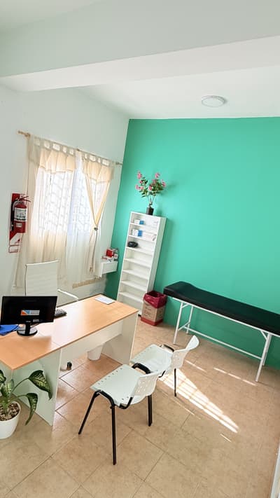 Consultorio con pared verde, escritorio y camilla